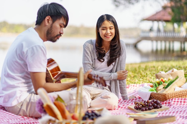 In coppia d'amore godendosi il tempo del picnic suonando la chitarra nel parco all'aperto Picnic coppia felice rilassante insieme al cestino da picnic