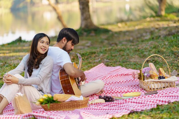 In coppia d'amore godendosi il tempo del picnic suonando la chitarra nel parco all'aperto Picnic coppia felice rilassante insieme al cestino da picnic