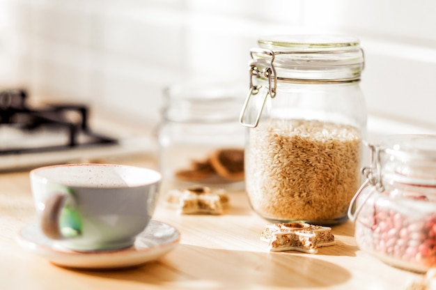 In cucina ci sono barattoli di riso e fagioli. Accanto alle lattine c'è una tazza da tè su un piattino e dei biscotti. Foto orizzontale