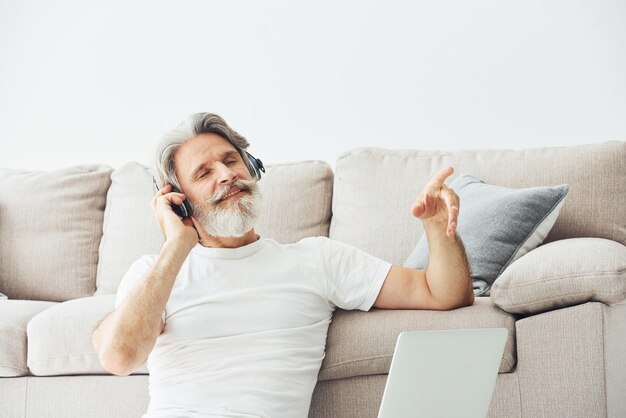 In cuffia Si siede vicino al divano Uomo moderno ed elegante con capelli grigi e barba all'interno