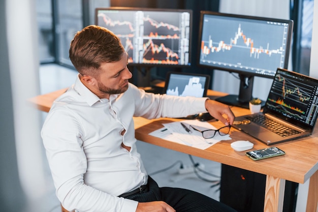 In formal clothes Young businessman is in office with multiple screens