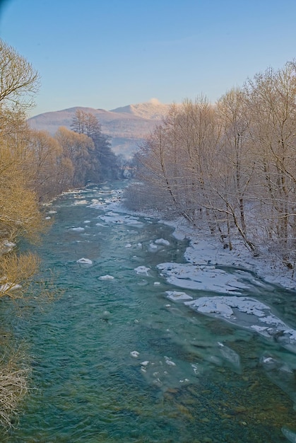 In inverno il letto del fiume non ghiacciato sullo sfondo invernale delle sponde innevate