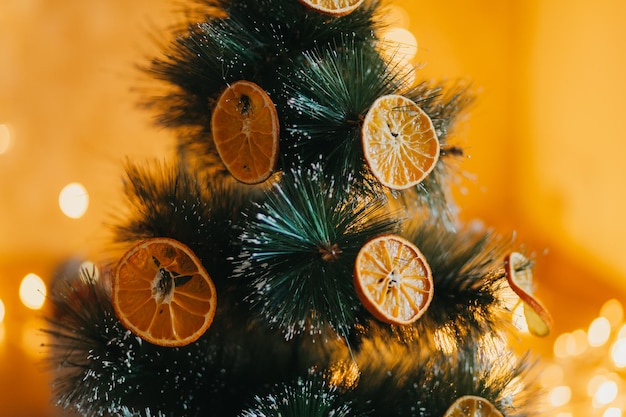 In inverno, l'albero è decorato con arance essiccate all'esterno, rami verdi su uno sfondo sfocato e bokeh giallo-oro. Decorazioni festive in stile ecologico. Buon Natale.