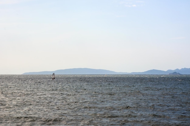 In lontananza un windsurfista galleggia sulle onde del mare Si possono vedere piccole montagne