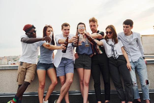 In piedi con l'alcol sul bordo del tetto Un gruppo di giovani in abiti casual fanno una festa insieme durante il giorno