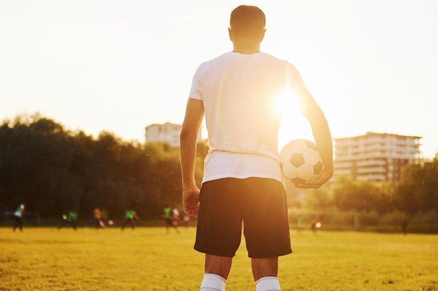 In piedi e tenendo la palla in mano Il giovane calciatore si allena sul campo sportivo