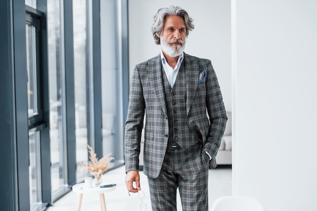 In piedi nella stanza Uomo moderno ed elegante con capelli grigi e barba all'interno