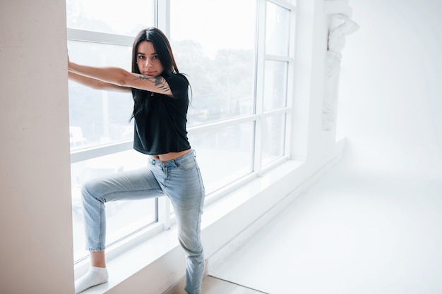 In piedi sul davanzale della finestra. La giovane teenager bruna femminile ha un servizio fotografico in studio durante il giorno