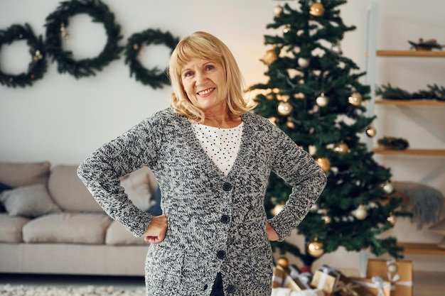 In piedi vicino all'albero di natale Senior donna con i capelli biondi è a casa