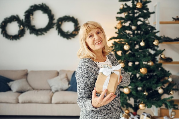 In piedi vicino all'albero di natale Senior donna con i capelli biondi è a casa