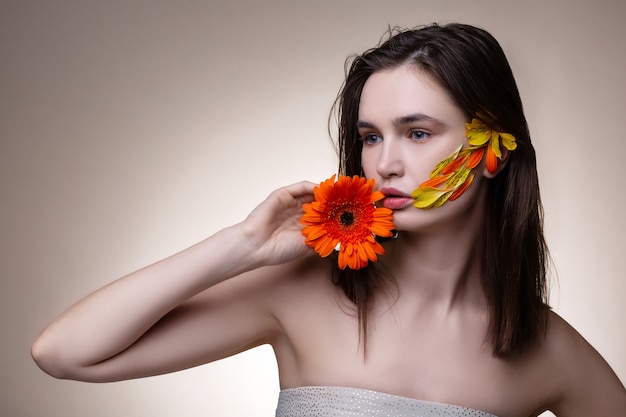 In posa con i fiori. Tenera giovane modella dai capelli scuri che indossa un abito a spalla aperta in posa con fiori