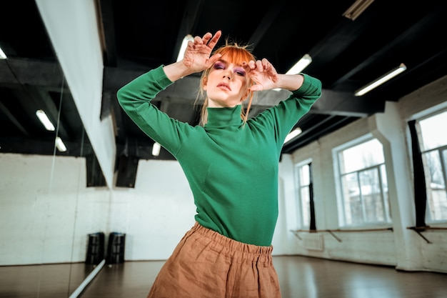 In posa per la foto. Giovane professionista dai capelli rossi che indossa un dolcevita verde in posa per la foto