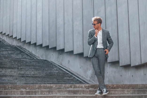 In posa per una macchina fotografica Giovane uomo d'affari in grigio abbigliamento formale è all'aperto in città