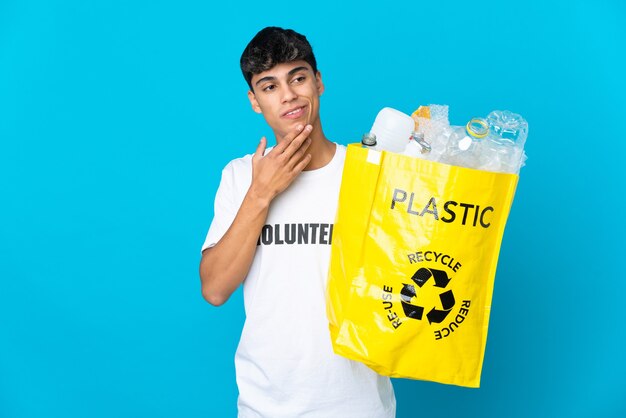 In possesso di un sacchetto pieno di bottiglie di plastica da riciclare nel blu alzando lo sguardo mentre sorride