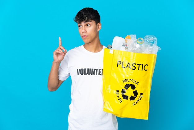 In possesso di un sacchetto pieno di bottiglie di plastica da riciclare sul blu pensando a un'idea che punta il dito verso l'alto