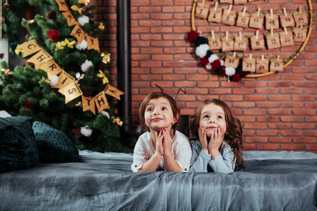 In previsione di regali. Cosa hanno Due allegre ragazzine sdraiate sul letto con decorazioni di Capodanno e albero delle vacanze