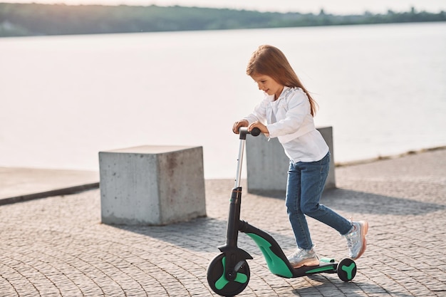 In sella al veicolo La bambina carina con lo scooter è all'aperto in estate