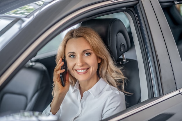 In una chiamata. Donna abbastanza bionda che parla su un telefono in una macchina