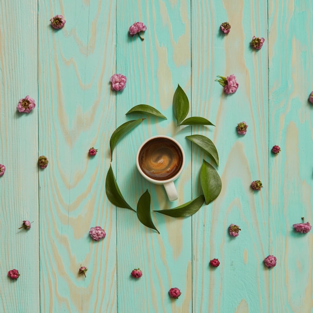 In una cornice rotonda con foglie e fiori rosa giaceva una tazza di caffè nero