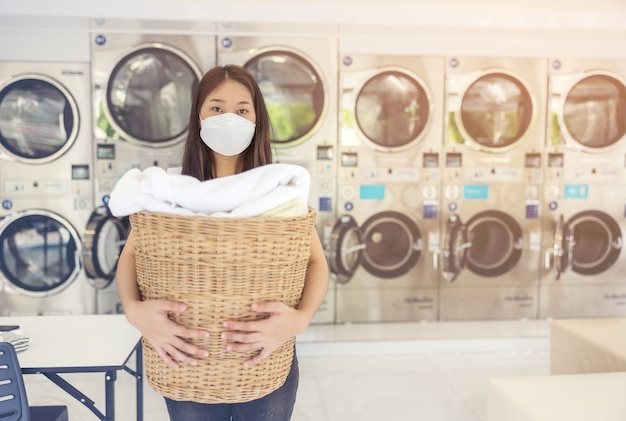 In una lavanderia a gettoni con molte lavatrici automatiche, una bella donna che indossa una maschera sta facendo il bucato.