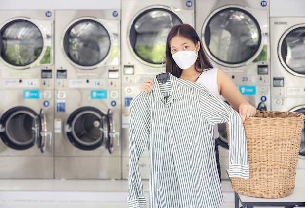 In una lavanderia a gettoni con molte lavatrici automatiche, una bella donna che indossa una maschera sta facendo il bucato.