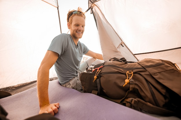 In una tenda. Un giovane in una tenda che sembra allegro seduto vicino al suo zaino