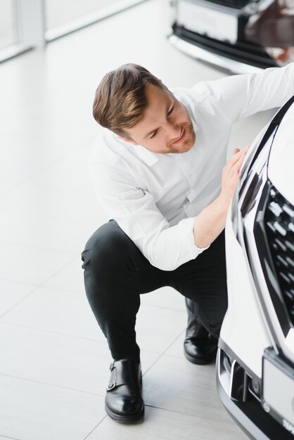 In visita alla concessionaria di automobili Bell'uomo barbuto sta accarezzando la sua nuova auto e sorridendo