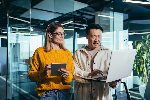 Incontro di lavoro di due dipendenti colleghe asiatiche e di sesso femminile che discutono del progetto lavorando in un ufficio moderno guardando lo schermo di un laptop discutendo le modifiche e il successo del progetto