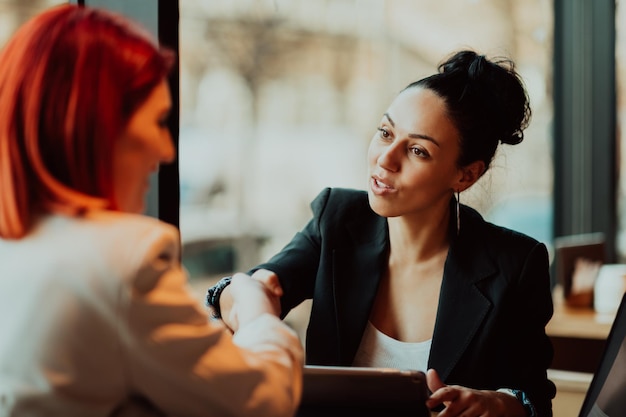 Incontro uno contro uno. Due giovani donne d'affari sedute al tavolo nel caffè. Ragazza che utilizza laptop, smartphone, blog. Lavoro di squadra, incontro di lavoro. Liberi professionisti che lavorano.