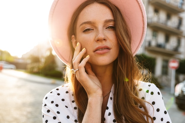 incredibile bella giovane donna rossa che cammina per strada all'aperto in abito e cappello.