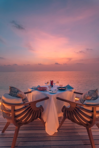 Incredibile cena romantica in coppia sulla spiaggia sul ponte di legno con candele sotto il cielo al tramonto. Romanticismo e amore