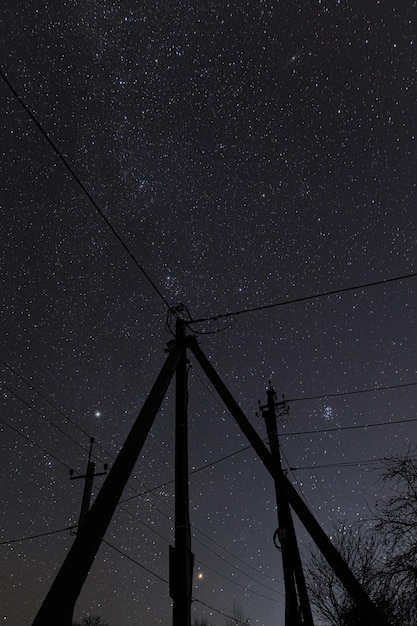 Incredibile cielo notturno con stelle e torri elettriche con linee in campagna Bel cielo stellato e cavi elettrici