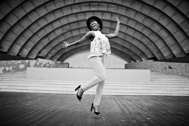 Incredibile donna modello afroamericano in pantaloni verdi e cappello nero poste all'aperto contro la sala dell'arena salta in aria