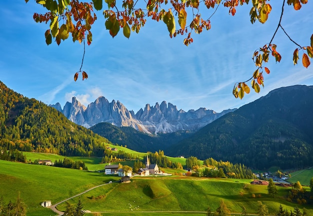 Incredibile scenario autunnale nel villaggio di Santa Maddalena con alberi colorati della chiesa e prati sotto i raggi del sole nascente Alpi Dolomitiche Italia