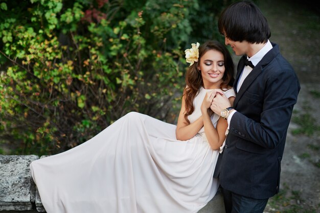 Incredibile sposa con lunghi capelli ricci e sposo in piedi vicino a vicenda a sfondo di foglie verdi, foto di matrimonio, bella coppia.