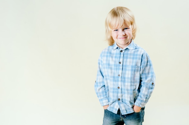 Incredibili occhi azzurri e innocenza di simpatici capelli biondi di un bambino di 5 anni. Semplice ritratto, che indossa una camicia blu, in piedi su uno sfondo bianco semplice. Isolato.