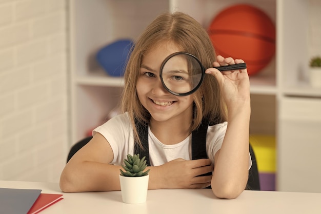 Indaga con la scienza della lente e la ragazza adolescente dell'infanzia che guarda la pianta attraverso la lente d'ingrandimento