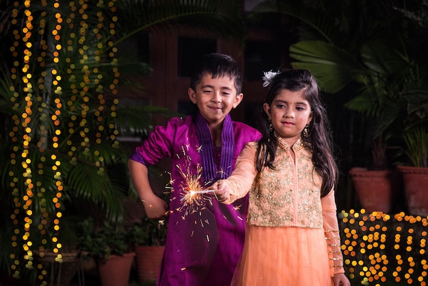 Indian carino ragazzo e ragazza in abiti tradizionali che giocano con stelle filanti o fulzadi o phuljhadi nella notte di diwali