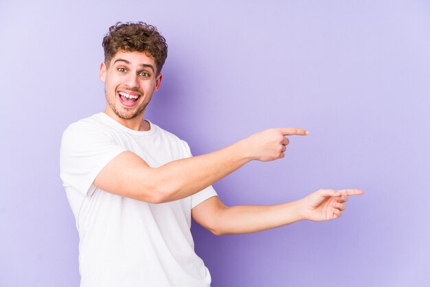 Indicare emozionante isolato giovane uomo caucasico dei capelli ricci biondi con gli indici di distanza.