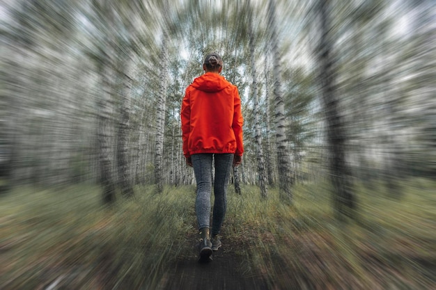 Indietro di una donna in giacca arancione che cammina su una strada sterrata nella foresta con stile di vita giacca rosa con