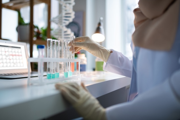 Indossa un camice bianco. Chimico che indossa camice bianco e guanti che lavorano in laboratorio con provette