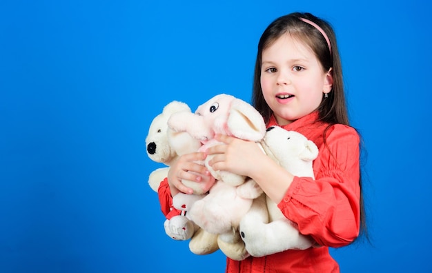 Infanzia felice Bambina gioca con un orsacchiotto di peluche Sacco di giocattoli nelle sue mani Collezionare giocattoli hobby Custodire i ricordi dell'infanzia Concetto di infanzia Piccola ragazza sorridente con i giocattoli