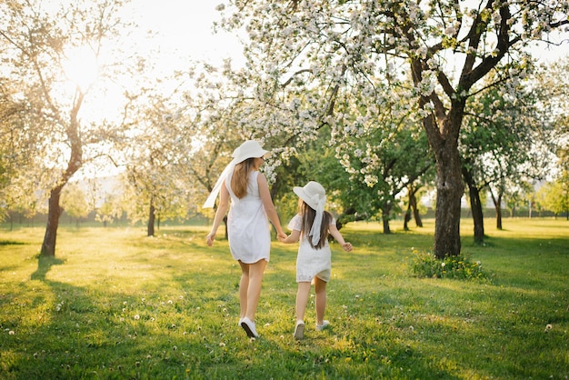 Infanzia felice con mamma la figlia tiene la mano di sua madre e corre con lei attraverso il giardino fiorito primaverile