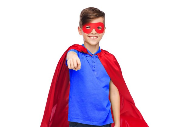 infanzia, gesto, costume di carnevale e concetto di persone - ragazzo felice con mantello da supereroe rosso e maschera che punta il dito verso di te