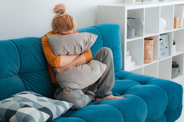 Infelice donna depressa sola a casa lei seduta sul divano nascondendo il suo concetto di depressione del cuscino del viso