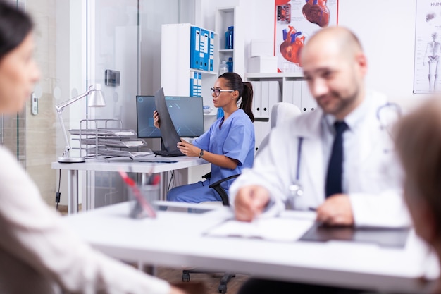 Infermiera che analizza la radiografia del paziente in una clinica privata mentre il medico consulta un'anziana in sedia a rotelle. Praticante che fa domande a una donna matura che compila il modulo di anamnesi della malattia, prescrivendo un trattamento