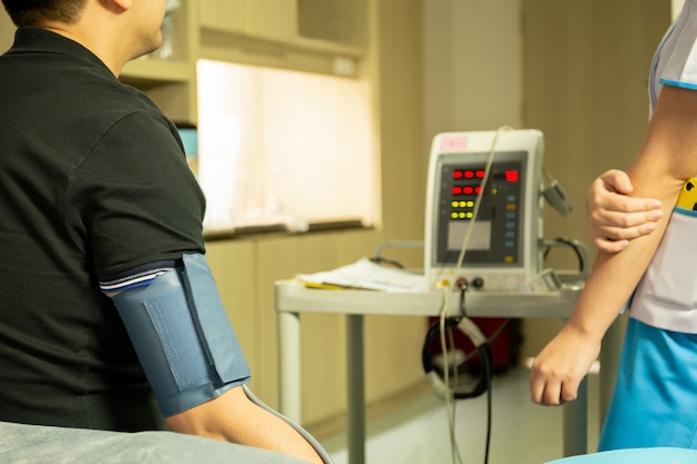 Infermiera che controlla pressione sanguigna sullo schermo di monitor per salute del paziente in ospedale.