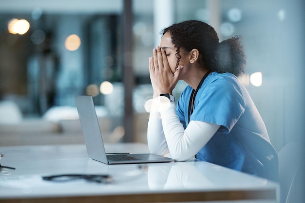 Infermiera da stress da burnout e donna di colore in ospedale che prova dolore stanco o malato durante il turno di notte Benessere sanitario e medico femminile con depressione o ansia mentre lavora fino a tardi sul laptop