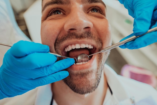 Infermiera donna dentista che controlla la bocca del paziente analizzando l'infezione dei denti utilizzando uno strumento trapano stomatologico durante l'esame ortodontico nella stanza dello studio dentistico. Concetto di procedura di odontoiatria. Q alta