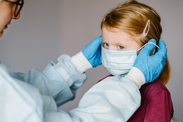 Infermiera, dottore in tuta protettiva, con maschera medica sul viso per bambino. Misure preventive contro l'infezione da Covid-19. Concetto di protezione contro l'influenza, epidemia di virus corona.